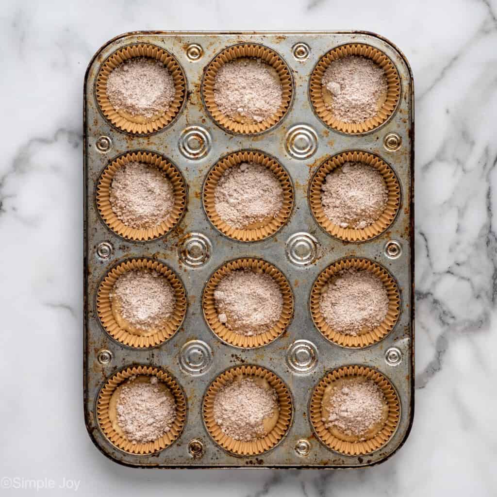 adding the filling of coffee cake muffins to muffin batter in a muffin tin
