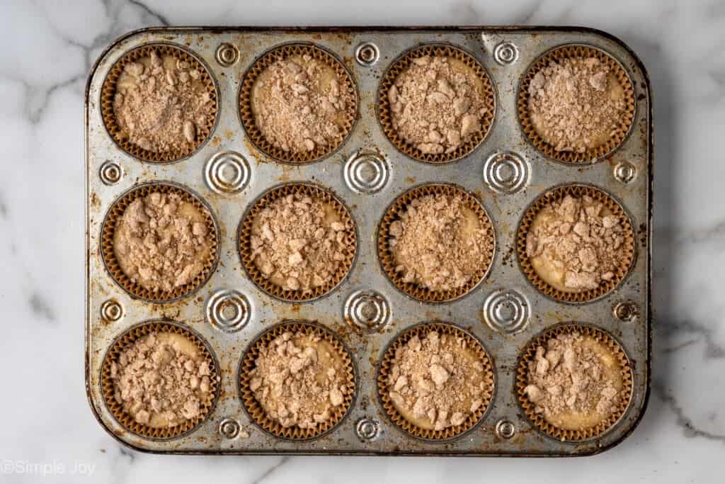 overhead of unbaked coffee cake muffins in a muffin tin in liners