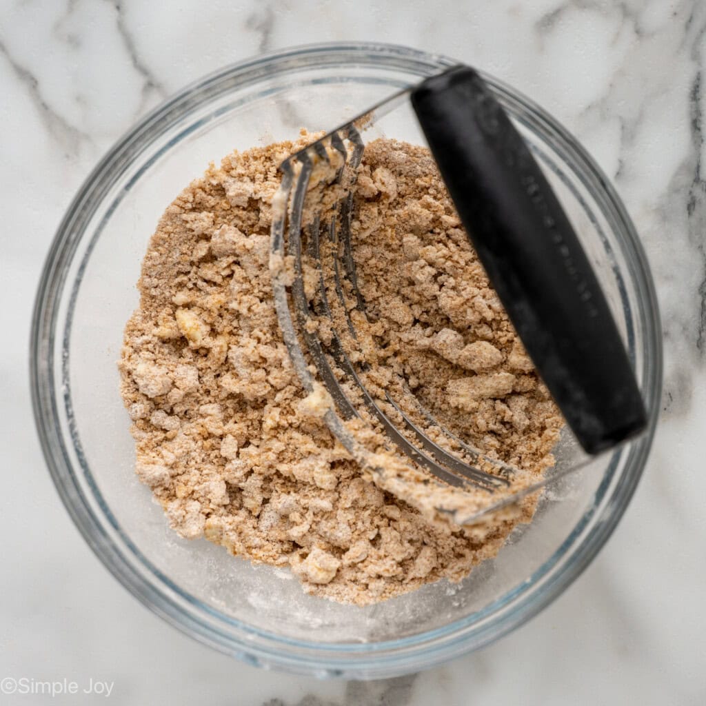 overhead of a bowl of streusel topping with a pastry cutter in it
