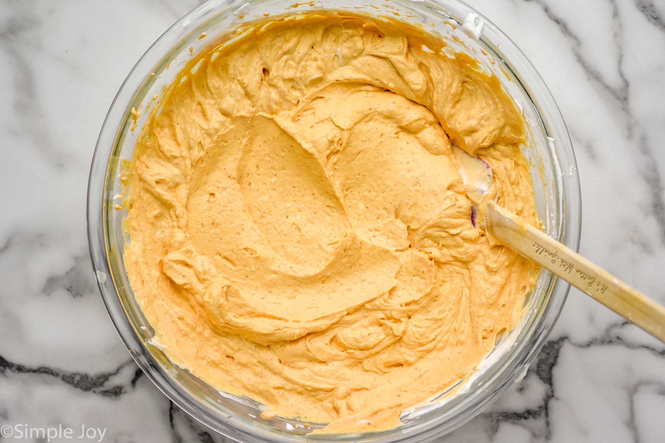 Overhead photo of a mixing bowl of ingredients and a mixing spoon for No Bake Pumpkin Cheesecake recipe.