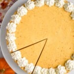 Overhead photo of No Bake Pumpkin Cheesecake on a cake plate with one slice cut. Pumpkins beside.