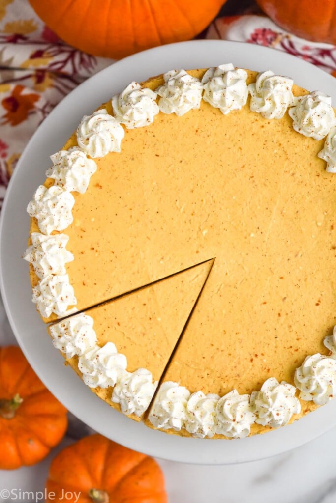 Overhead photo of No Bake Pumpkin Cheesecake on a cake plate with one slice cut. Pumpkins beside.