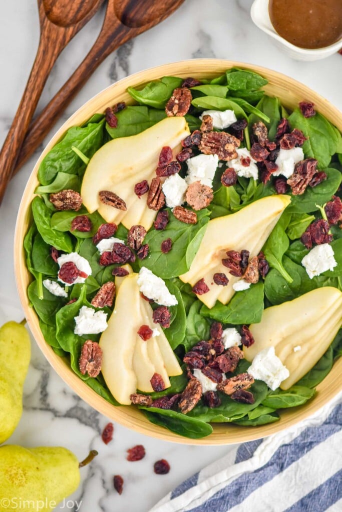 Overhead view of bowl of Pear Salad before dressing is added. Salad tongs, pairs, and dressing beside.