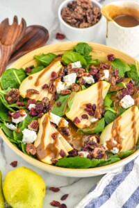 Bowl of Pear Salad. Pears, salad tongs, candied nuts, and dressing beside.