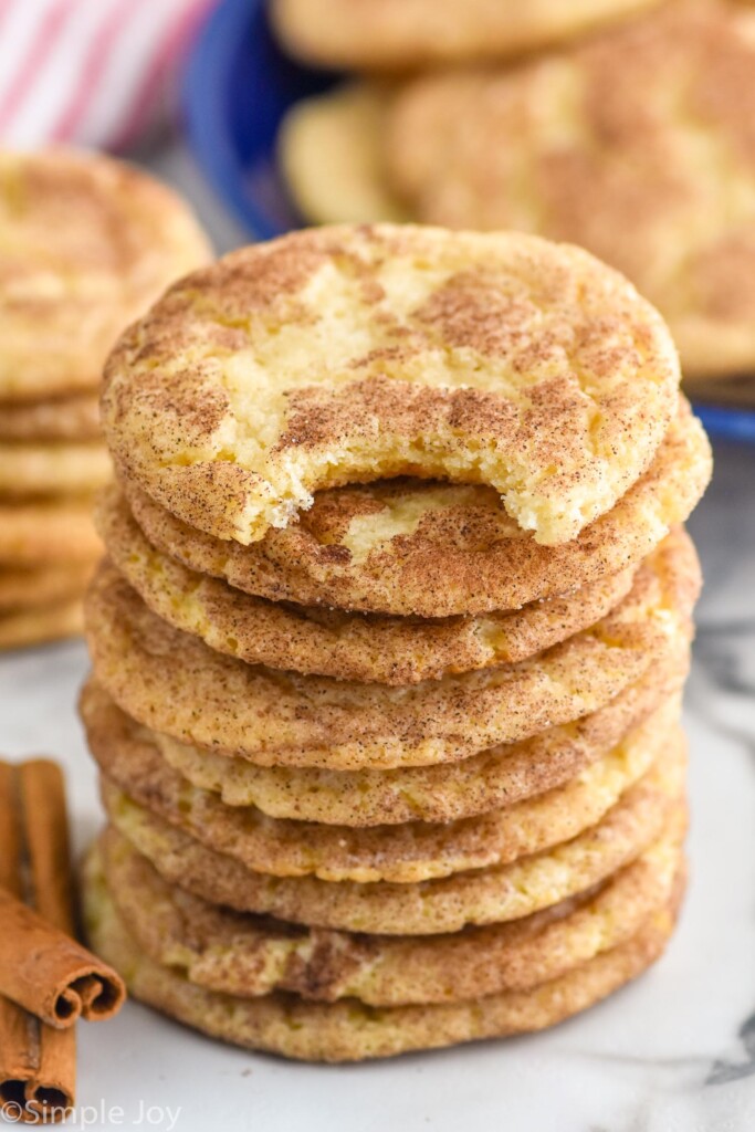 Stack of Snickerdoodles with a bite taken out of the top cookie. Cinnamon sticks beside.