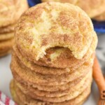 Stack of Snickerdoodles with a bite taken out of the top cookie. Cinnamon sticks and more Snickerdoodles beside.