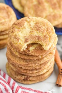 Stack of Snickerdoodles with a bite taken out of the top cookie. Cinnamon sticks and more Snickerdoodles beside.