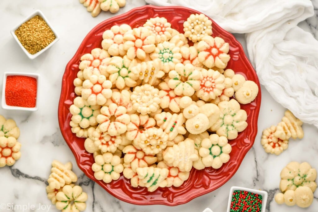 Overhead photo of decorated Spritz Cookies on a platter. More cookies and sprinkles beside.