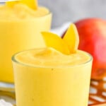 Pinterest graphic for Mango Smoothie recipe. Text says, "the best Mango Smoothie simplejoy.com." Image shows Mango Smoothie with mango slices. More mango slices and a whole mango beside.