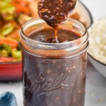 Photo of spoonful of Stir Fry Sauce over jar of Stir Fry Sauce with stir fry in skillet and bowl of rice in the background. - 8