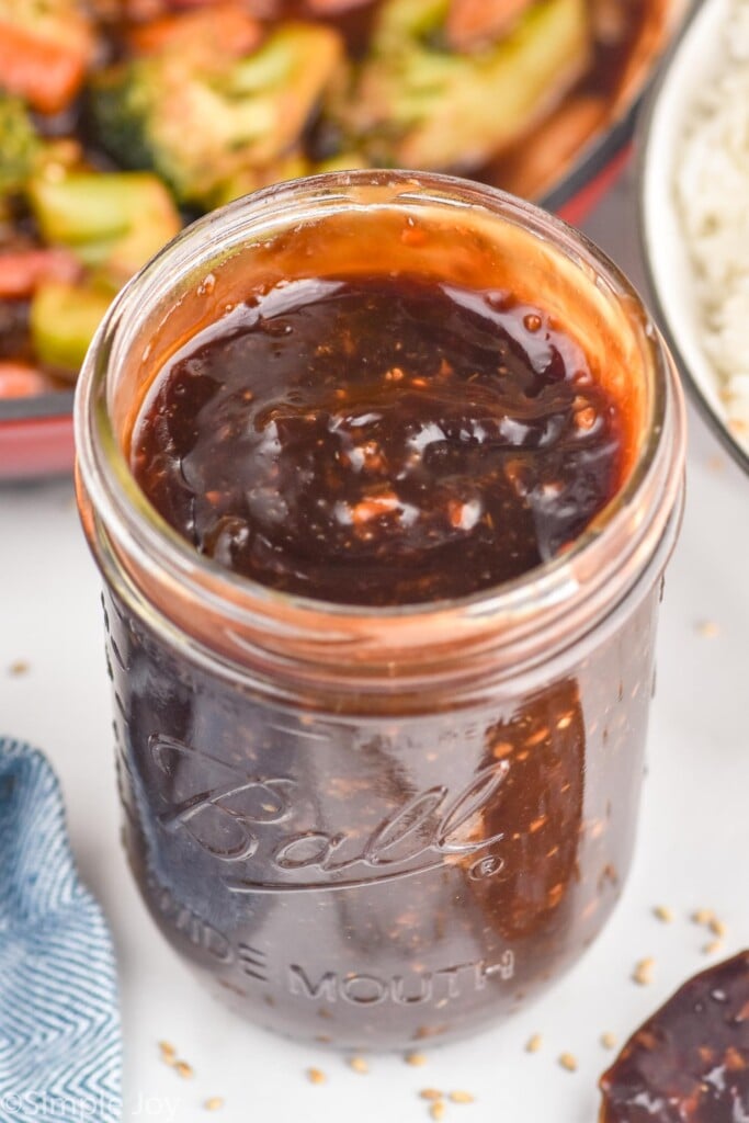 Jar of Stir Fry Sauce with skillet of stir fry in bowl of rice behind.