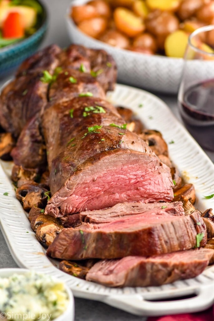 beef tenderloin on a platter with potatoes and salad sitting in background