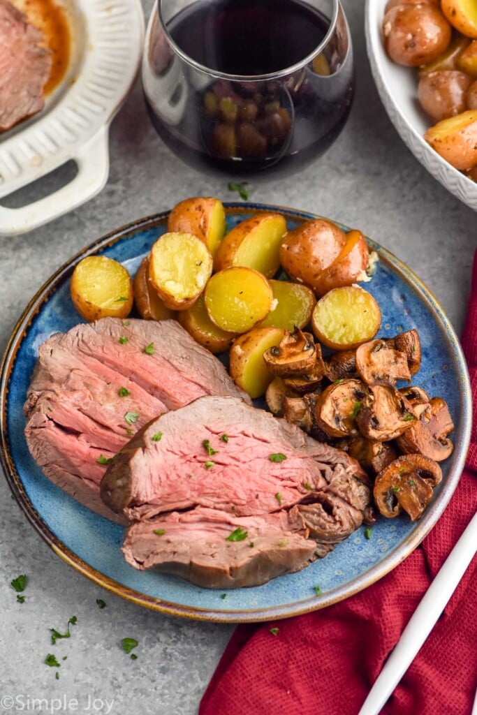 plate of beef tenderloin, mushrooms, and potatoes. Glass of wine and platters of food sitting in background