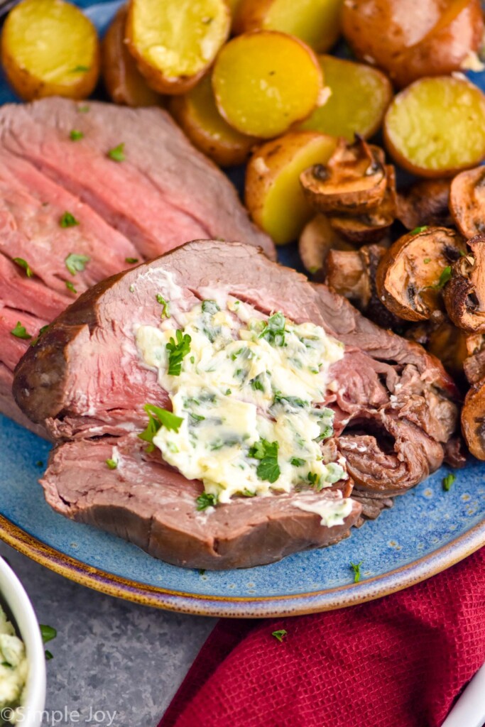 beef tenderloin with herby butter with potatoes and mushrooms sitting beside