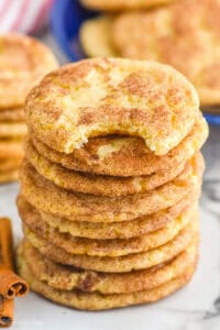 Stack of Snickerdoodles with a bite taken out of the top cookie. Cinnamon sticks beside.