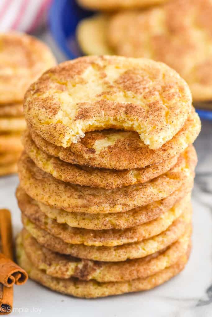 Stack of Snickerdoodles with a bite taken out of the top cookie. Cinnamon sticks beside.