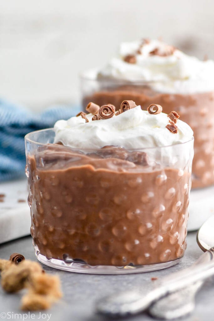 Side view of cups of Chocolate Pudding garnished with whipped cream and chocolate shavings. Spoons beside.