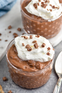 Two bowls of Chocolate Pudding garnished with whipped cream and chocolate shavings. Spoon beside.
