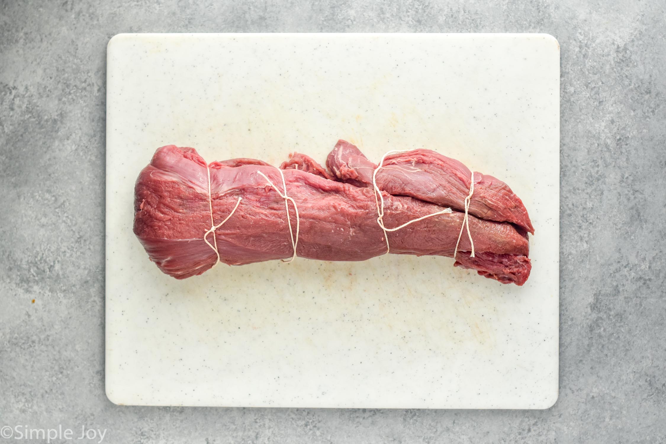 overhead of a beef tenderloin tied with twine on a cutting board
