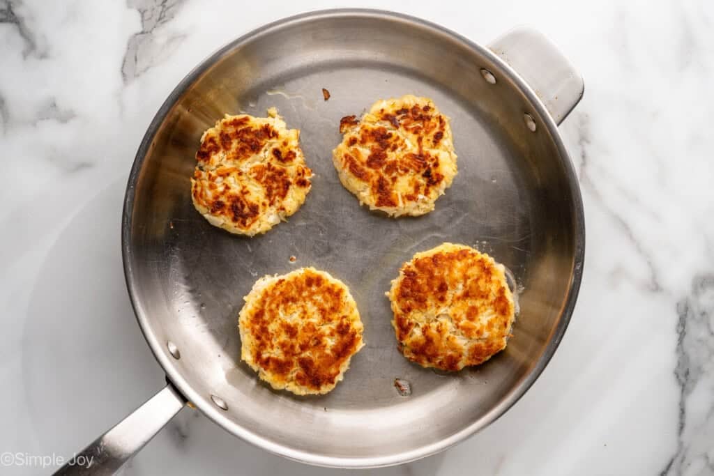 overhead of four crab cakes in a frying pan