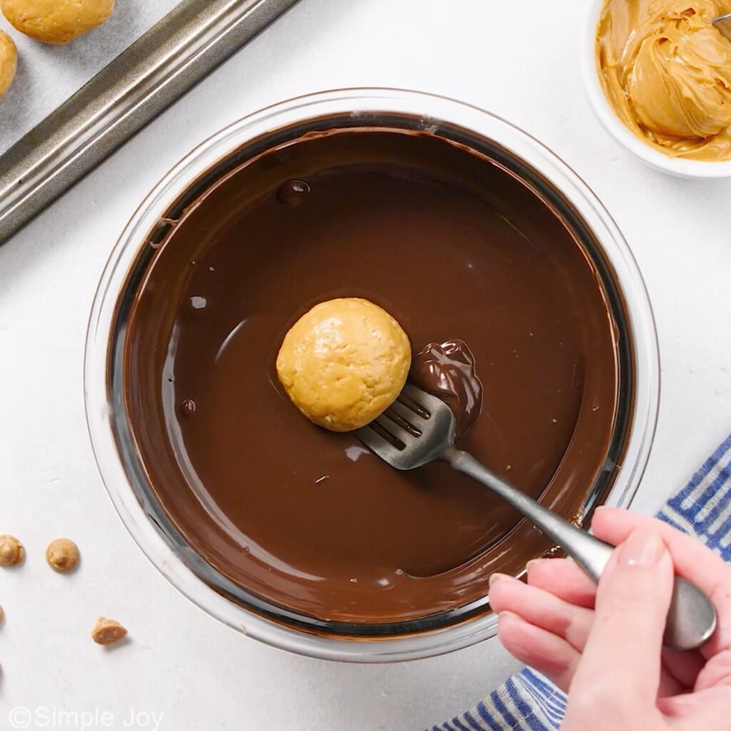 a fork lowering a peanut butter ball into melted chocolate