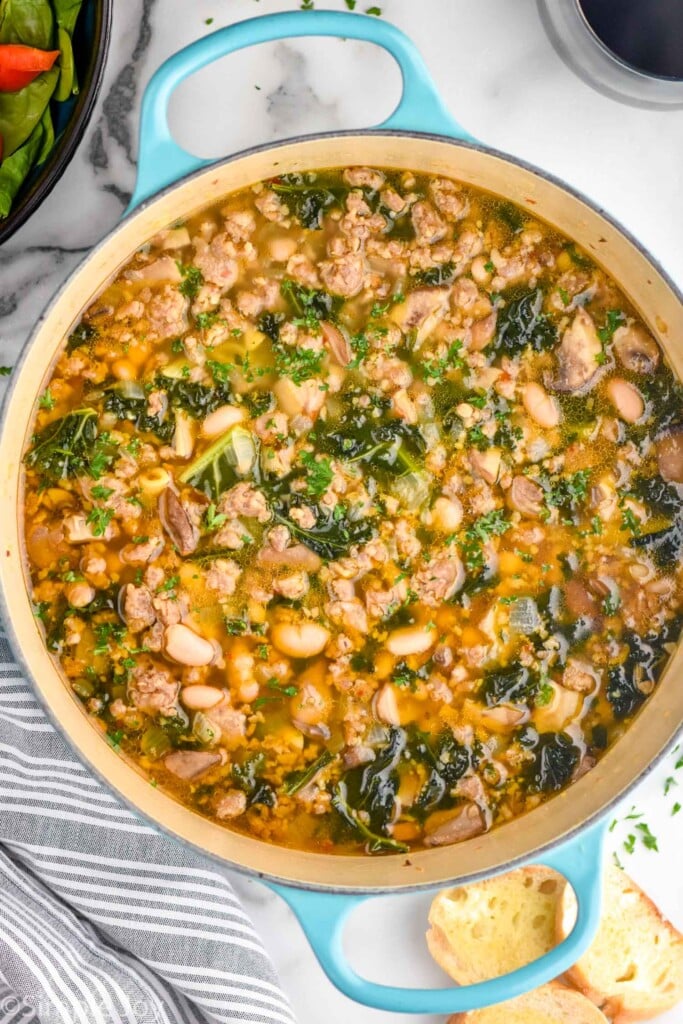 Overhead photo of a pot of sausage and kale soup with bread and glass of wine beside.