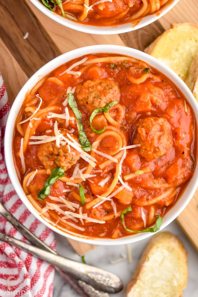 Overhead view of bowls of Meatball Soup with bread and spoons beside.