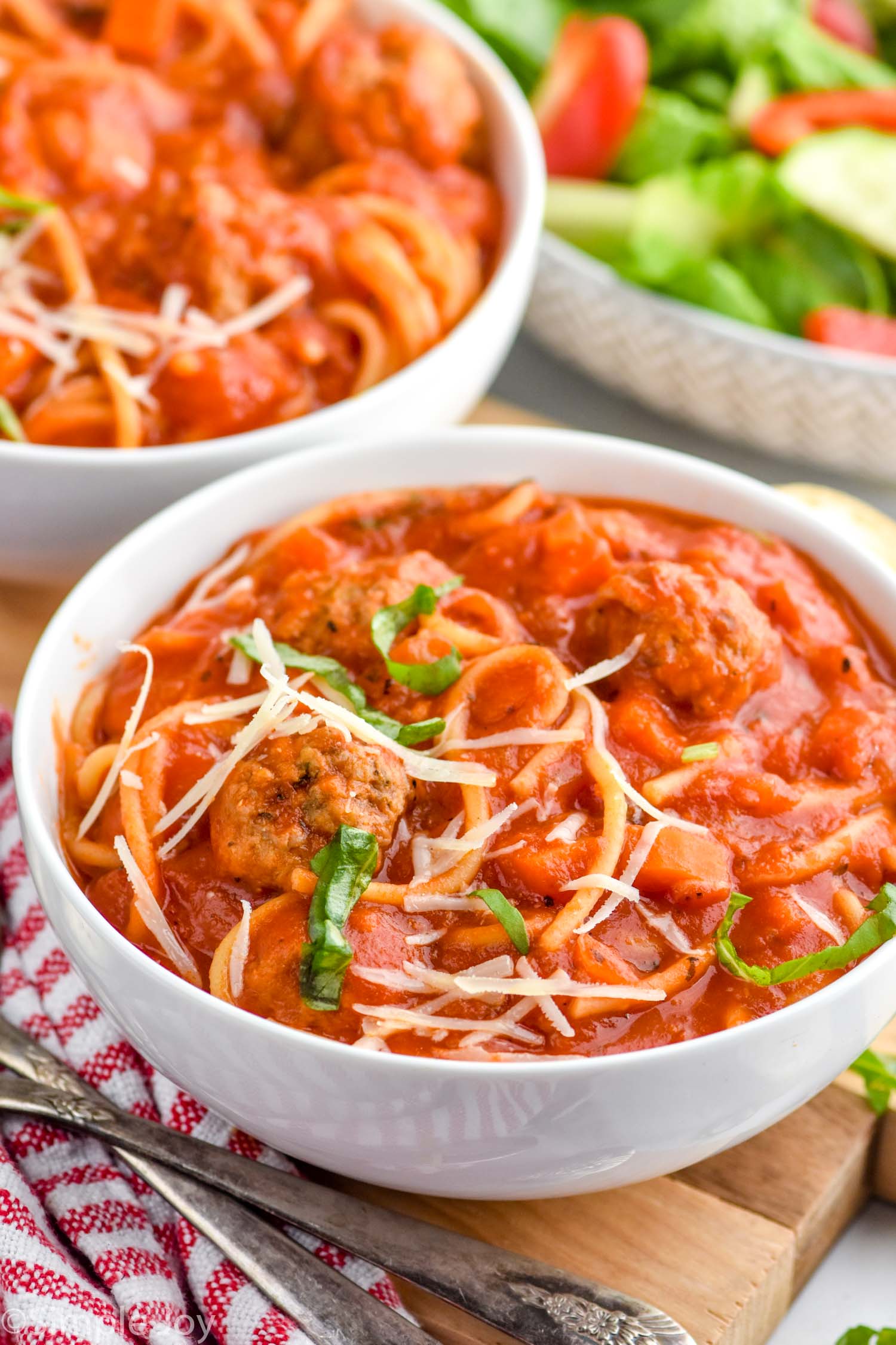 Bowls of Meatball Soup with salad and spoons beside.