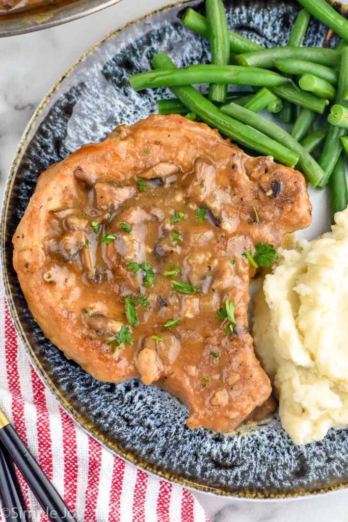 smothered pork chop on a plate with green beans and mashed potatoes
