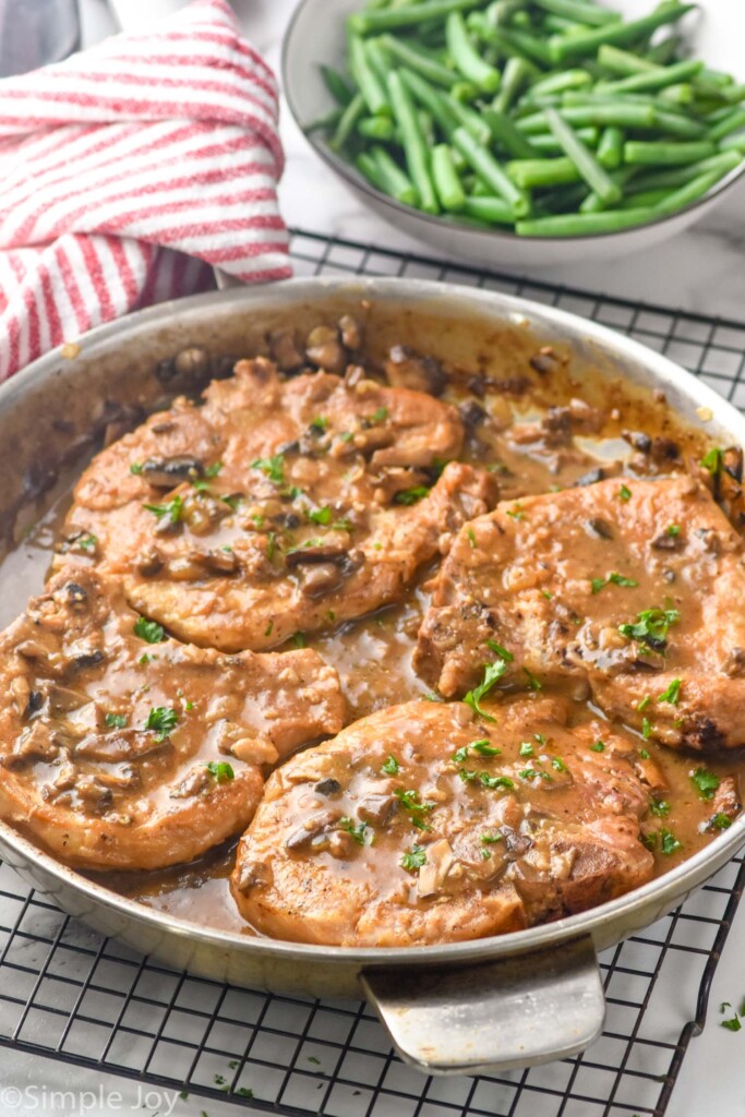 pan of smothered pork chops. Bowl of green beans sitting in background