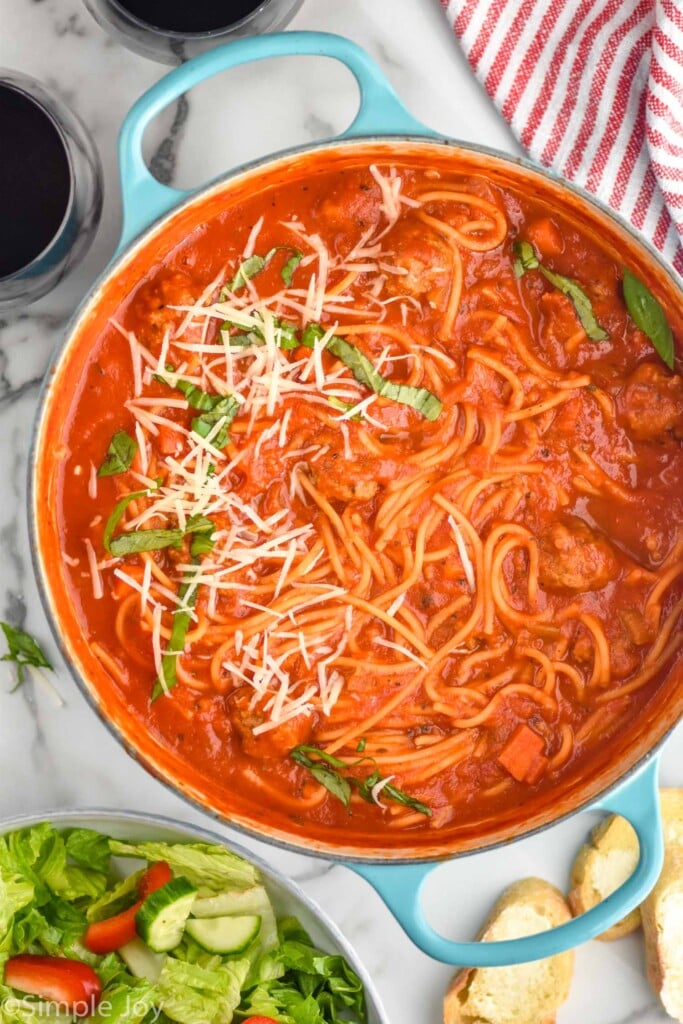 Overhead view of a pot of Meatball Soup with salad, bread, and wine beside.