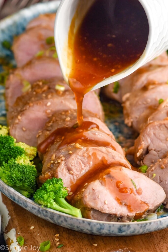 Marinade being poured over sliced Teriyaki Pork Tenderloin on a platter with broccoli.