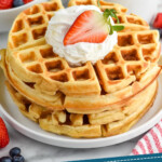 Pinterest graphic for Buttermilk Waffles recipe. Image shows a stack of Buttermilk Waffles on a plate, garnished with whipped cream and a strawberry. Cups of coffee and bowl of berries beside. Text says, "tried & tested Buttermilk Waffles simplejoy.com"