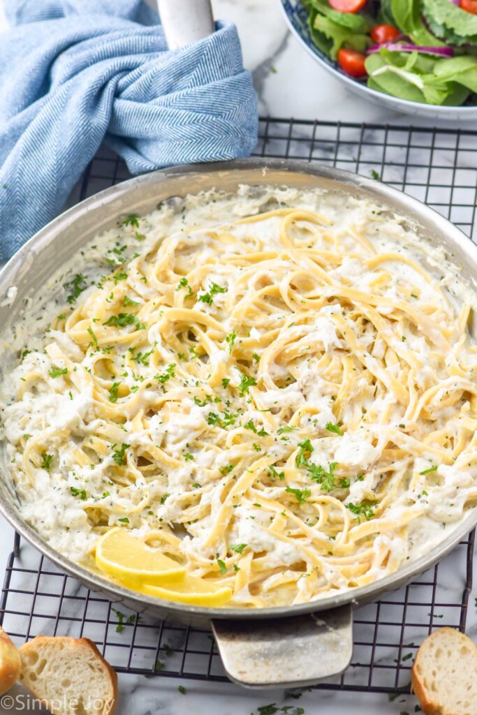 Photo of a skillet of Creamy Crab Pasta on a cooling rack. Bowl of salad and slices of bread beside.