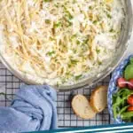 Pinterest graphic for Creamy Crab Pasta recipe. Image shows overhead view of a skillet of Creamy Crab Pasta with lemon slices on a cooling rack. Slices of bread and bowl of salad beside. Text says, "crab pasta simplejoy.com"