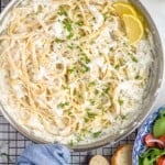 Overhead view of a skillet of Creamy Crab Pasta with lemons on a cooling rack. Slices of bread and bowl of salad beside. - 11