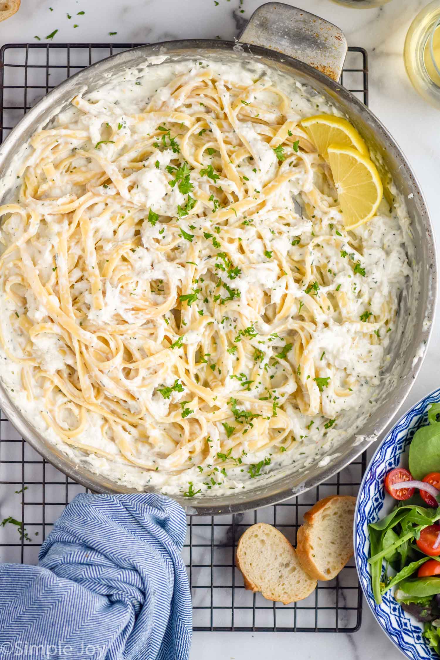 Overhead view of a skillet of Creamy Crab Pasta with lemons on a cooling rack. Slices of bread and bowl of salad beside.