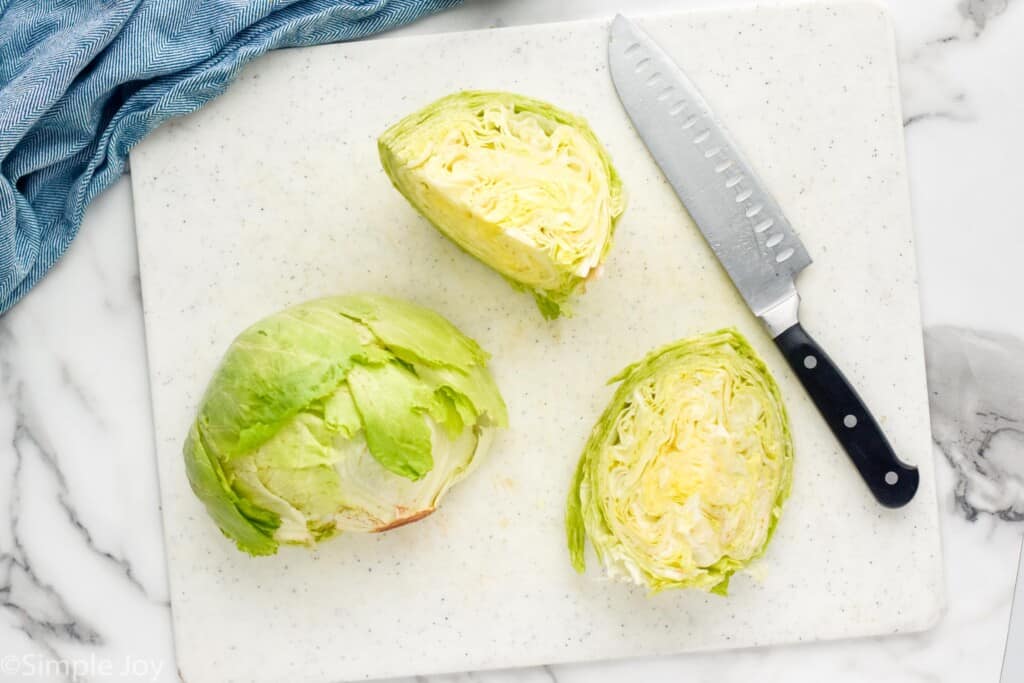 Overhead photo of a head of lettuce cut into three pieces on a cutting board with a knife for Wedge Salad recipe.