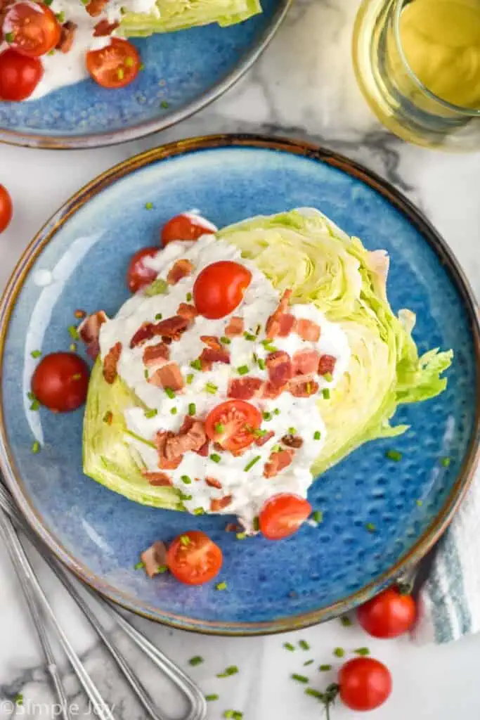 Overhead photo of Wedge Salad on a plate with another Wedge Salad and glass of white wine beside.