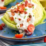 Pinterest graphic for Wedge Salad recipe. Image shows Wedge Salad served on a plate with dressing, tomatoes, and bacon. Another Wedge Salad and glasses of wine beside. Text says, "Wedge Salad simplejoy.com."
