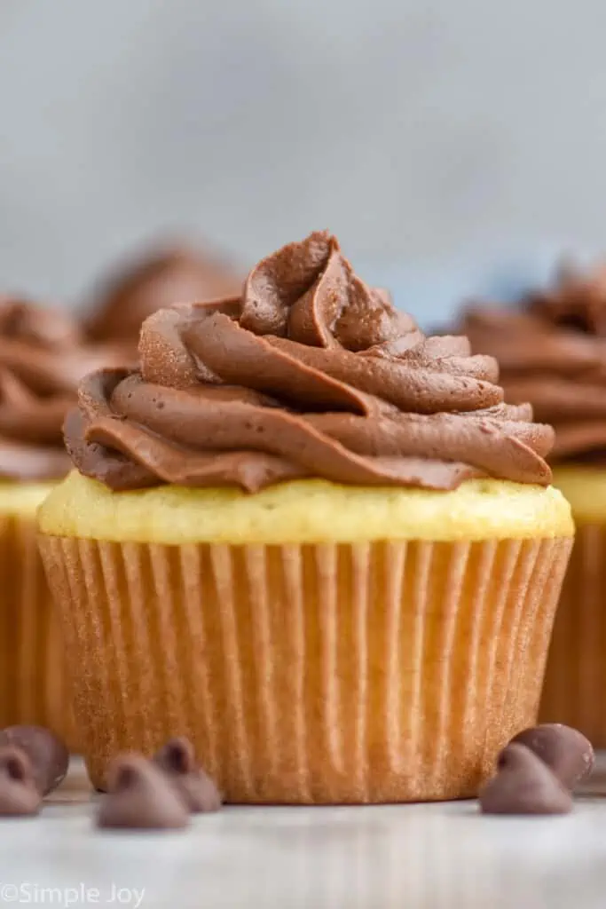 Side view of cupcakes topped with Chocolate Cream Cheese Frosting. chocolate chips beside.