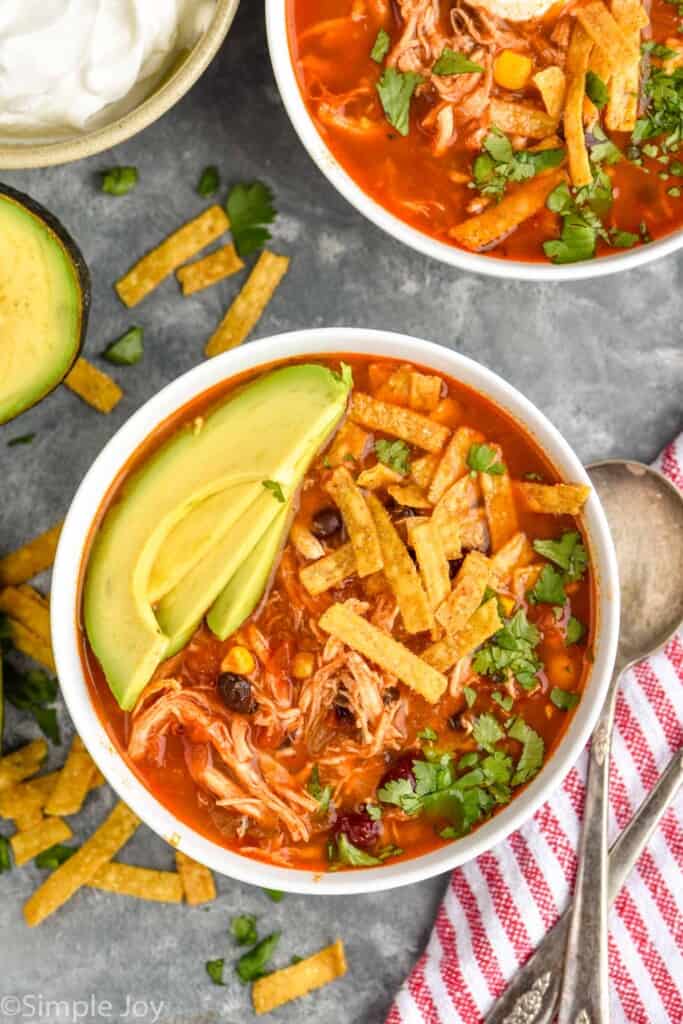 Overhead view of bowls of Chicken Tortilla Soup garnished with slices of avocado. Spoons beside.