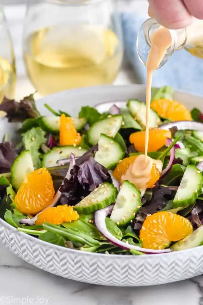 man's hand pouring ginger dressing over bowl of salad