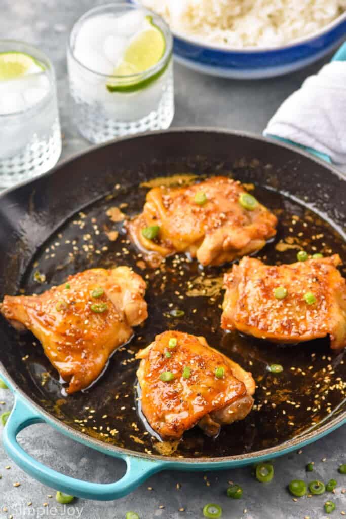 Honey Garlic Chicken Thighs in a skillet with drinks and rice beside