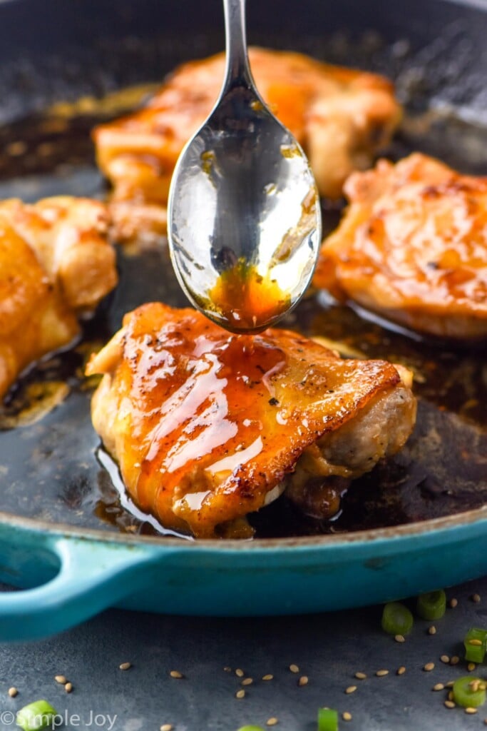 Spoon of sauce being drizzled on chicken in skillet for Honey Garlic Chicken Thighs recipe