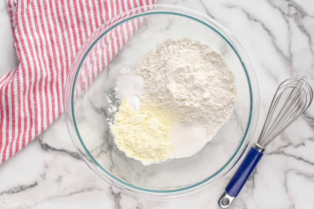 Overhead view of a mixing bowl of ingredients for Buttermilk Waffles recipe. Wisk and towel beside.