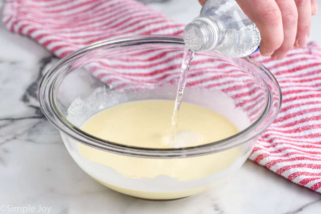Photo of person's hand pouring club soda into mixing bowl of ingredients for Buttermilk Waffles recipe.