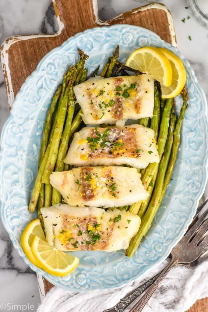 Overhead photo of a platter of Air Fryer Cod, asparagus, and lemon slices.
