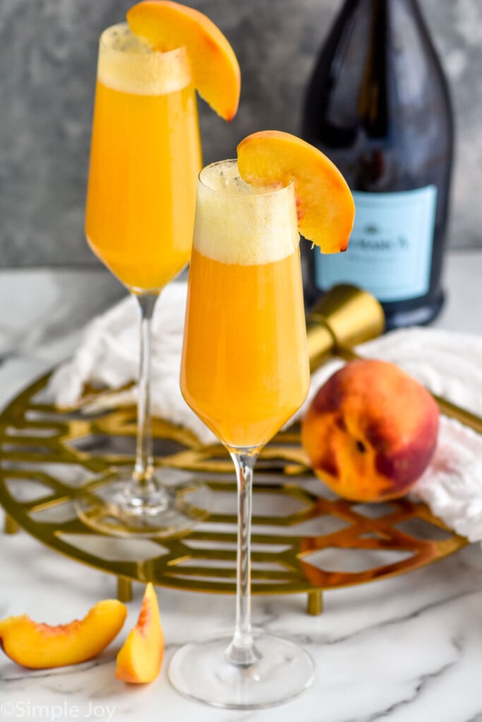 Bellinis with peach and peach slices beside. Bottle of champagne beside.