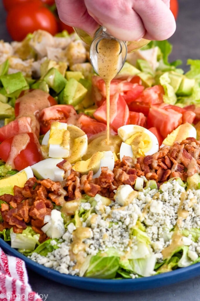 Person's hand pouring dressing onto Cobb Salad